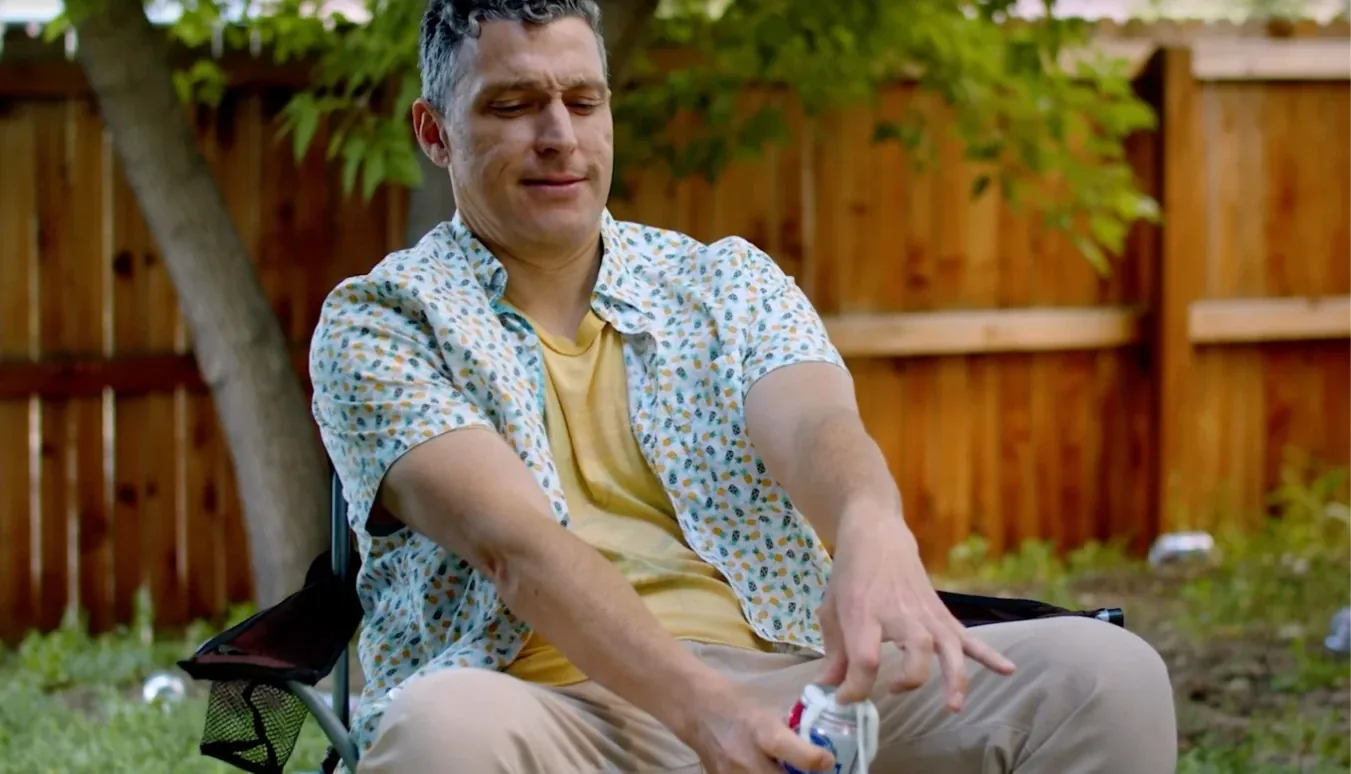 Actor wincing in a camp chair in a backyard, from Mark Markus & the Shark Carcass